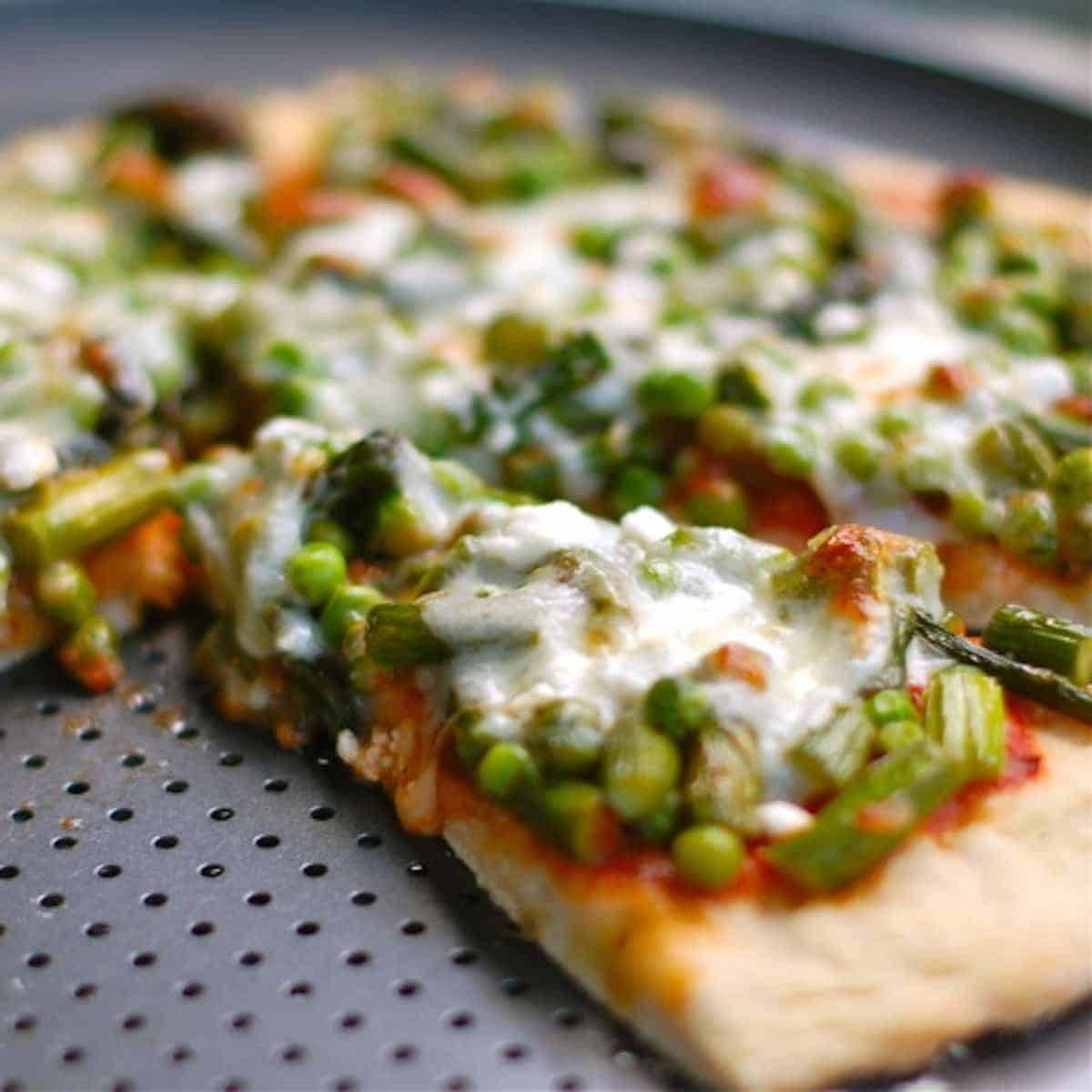 Asparagus, peas, and goat cheese pizza on a pizza platter.