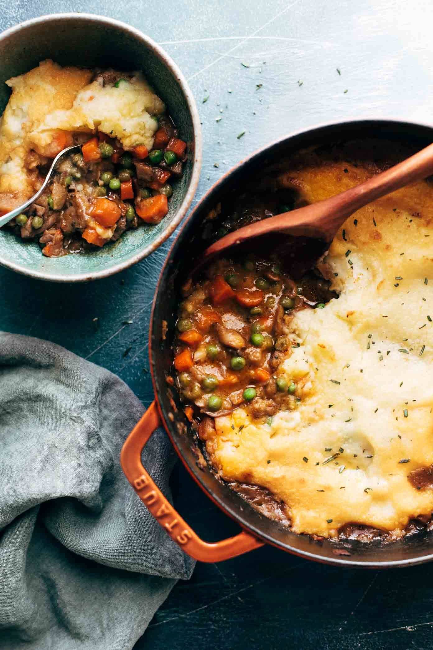 Vegetarian Shepherd's Pie in a red casserole dish being scooped with a wooden spoon