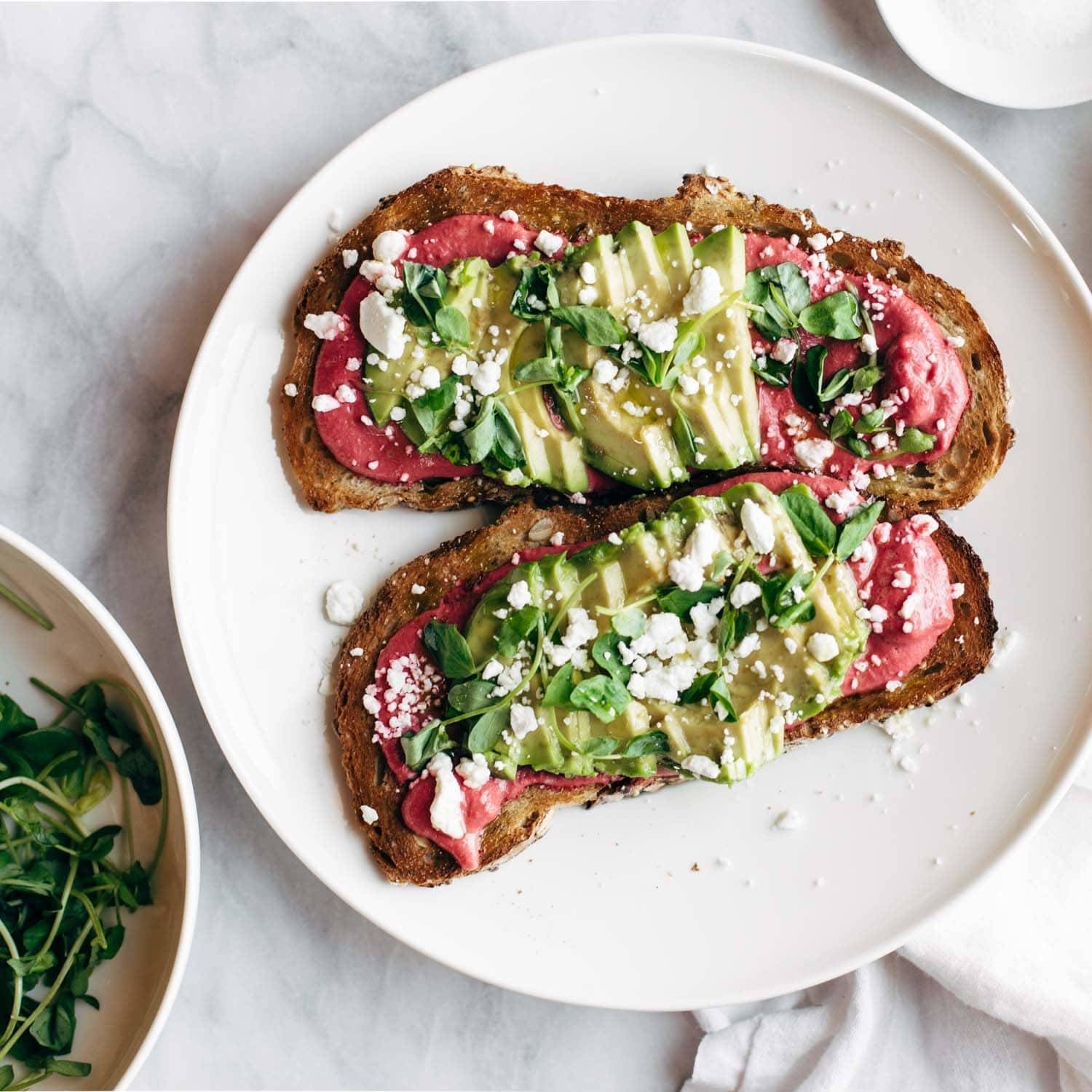 Toast on a white plate with avocado and cheese toppings.