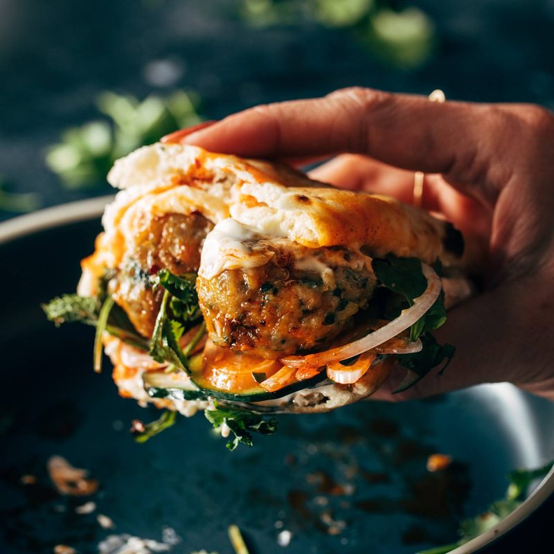 White hand holding a ginger chicken meatball sandwich